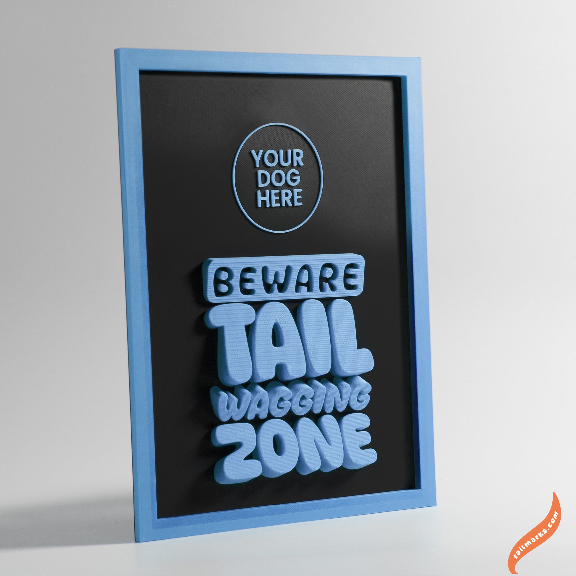 Decorative sign with text 'Beware Tail Wagging Zone' in a blue frame on a light gray background.