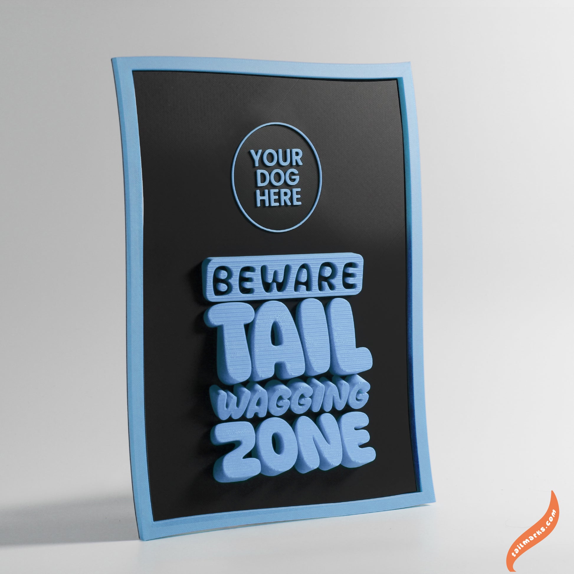 Black sign with blue text 'Beware Tail Wagging Zone' with a waggy frame on a gray background