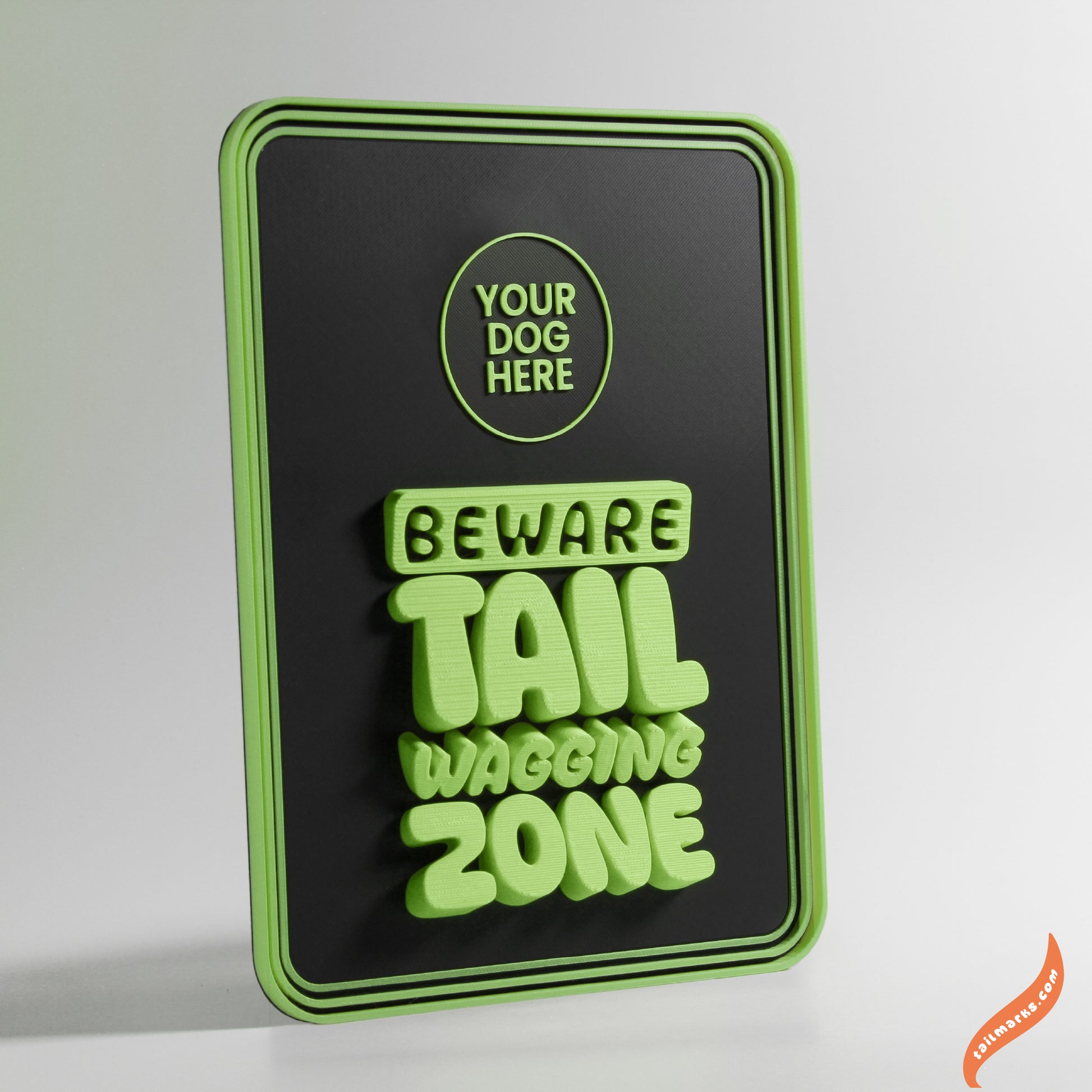 Green and black sign with text 'Beware Tail Wagging Zone' with a round frame on a grey background