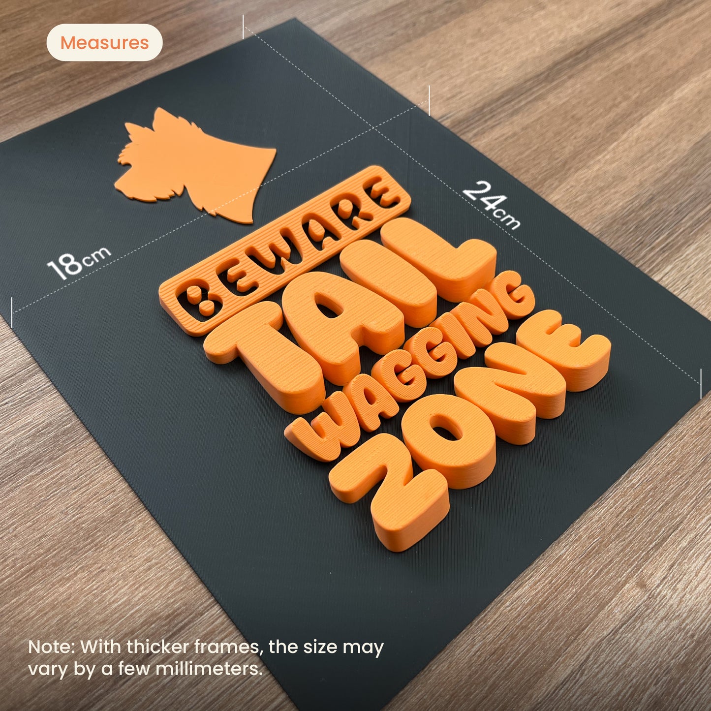 Orange beware tail wagging zone text and dog shape on a black mat with measurements on a wooden floor.
