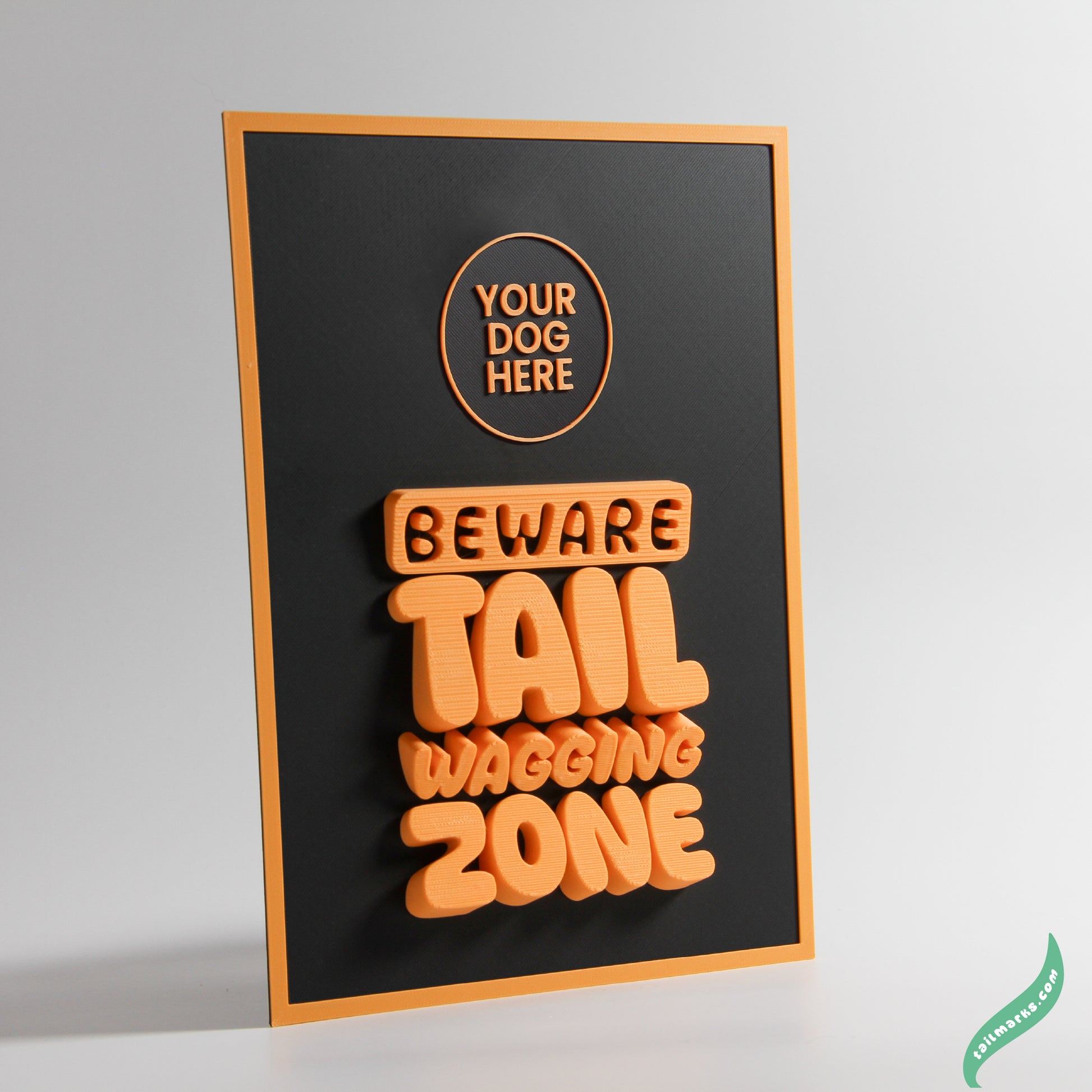 Decorative sign with text 'Beware Tail Wagging Zone' on a black background and a sli orange frame