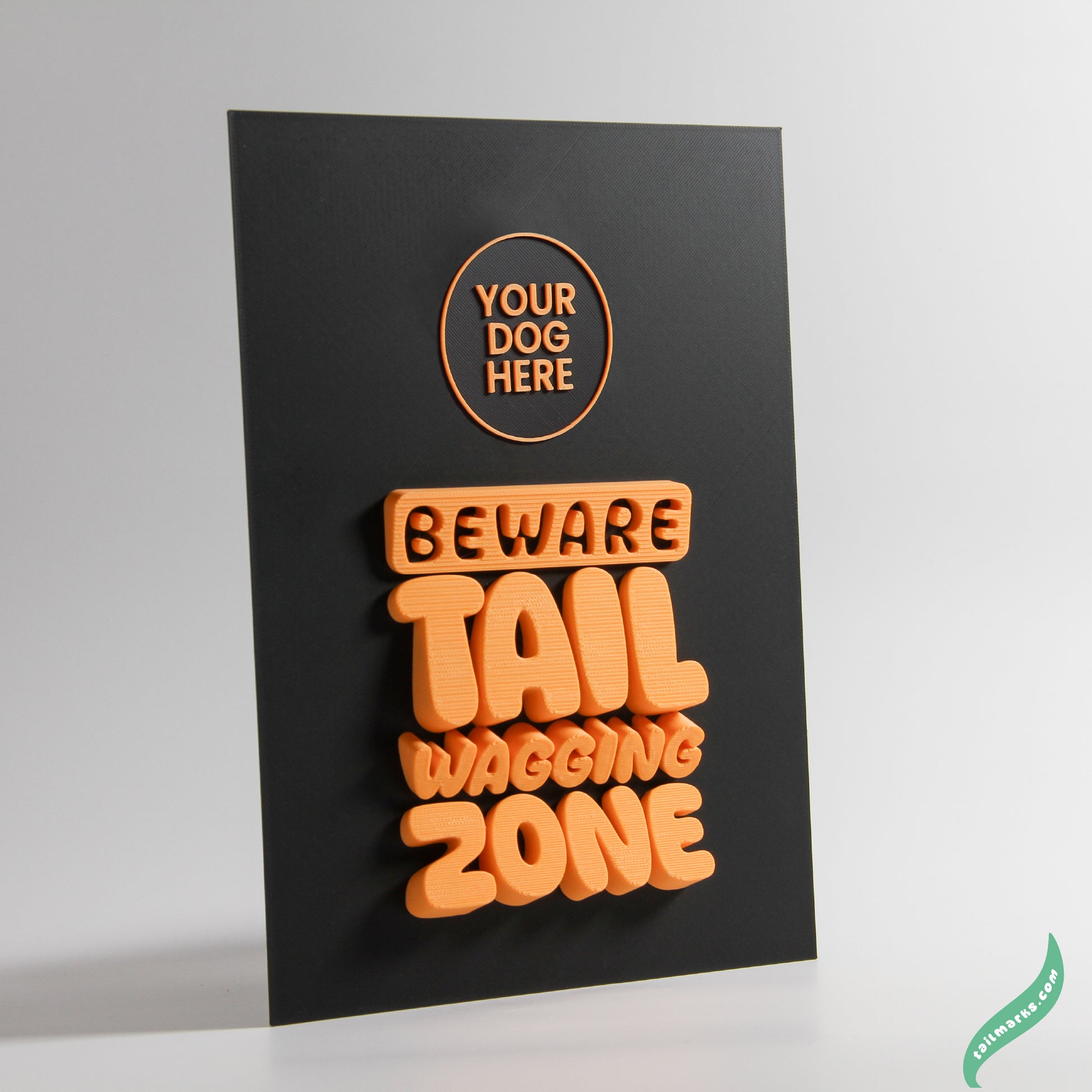 Black sign with orange text 'Beware Tail Wagging Zone' on a white background