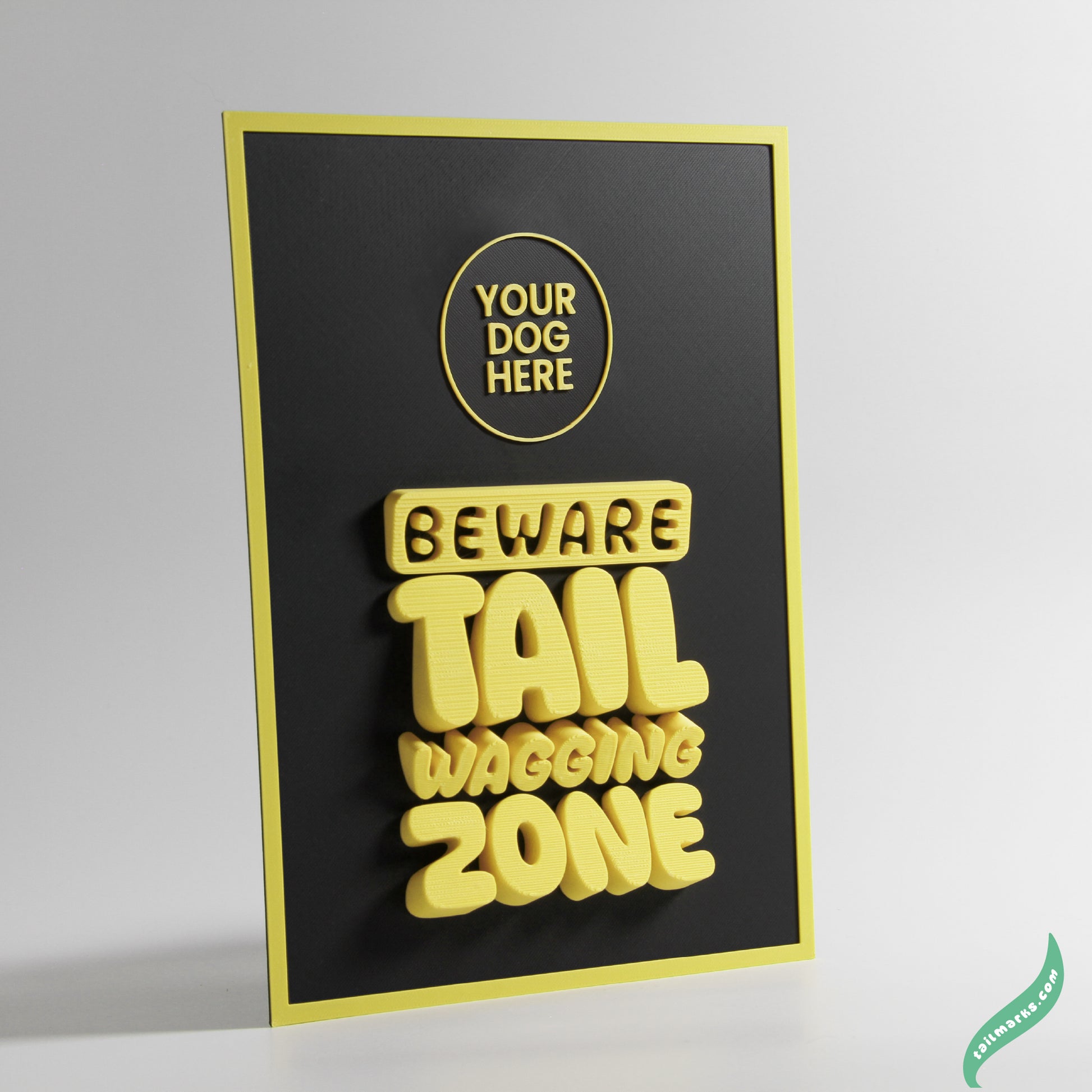 Black sign with yellow text 'Beware Tail Wagging Zone' on a white background with a slim frame
